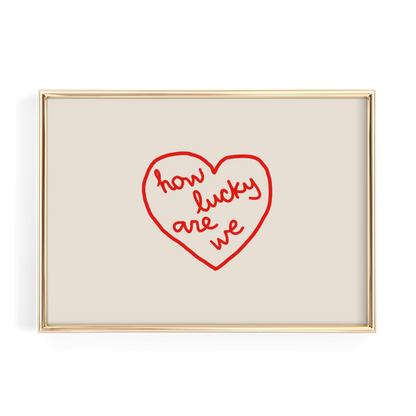 A framed image with a red heart-shaped design containing the text "how lucky are we" written in cursive.