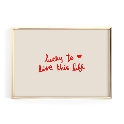 a framed piece of art with the text "lucky to live this life" written in red cursive font.