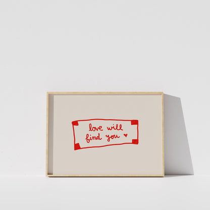 A simple white wall with a framed piece of art featuring the text "love will find you" in red.