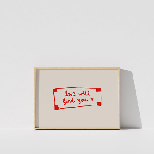 A simple white wall with a framed piece of art featuring the text "love will find you" in red.