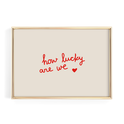 A gold-framed picture with a beige background and the text "how lucky are we" written in red cursive.